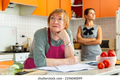 Offended Elderly Woman With Worried Adult Daughter Reprimanding Her Sitting At Home Kitchen