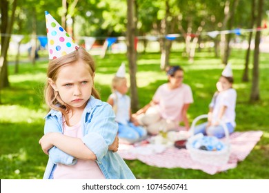 Offended littlee child hugging herself and scowling on background of other people enjoying picnic in park on summer day - Shutterstock ID 1074560741