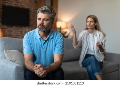 Offended Unhappy Mature Caucasian Woman Scolds At Sad Husband, Man Ignores Wife In Living Room Interior, Free Space. Relationships Problems, Family Crisis, Quarrel At Home, Abuse, Divorce And Break