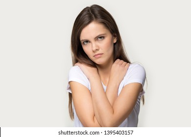 Offended Vulnerable Sad Millennial Girl Looks At Camera Pose Over Grey Studio Background Self Hug Closed Pose Folded Crossed Arms On Chest, Woman Feels Lonely Cheated Suffering From Bullying Or Abuse