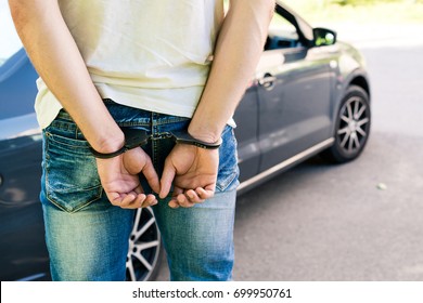 an offender standing in handcuffs near the car. Concept of arrest the driver, violation of rules and drinking alcohol while driving the car