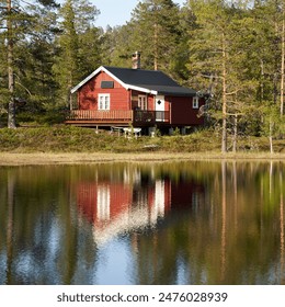 Off-grid, sun-powered, small traditional red wooden cabin by a small lake in Norway during the summer - Powered by Shutterstock