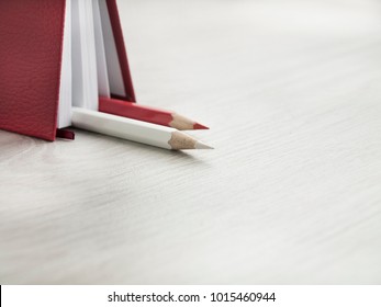 Office accessories: a red notepad, a white pencil and red pencil on a wooden gray desk. Back to school. Top view. Copy space.