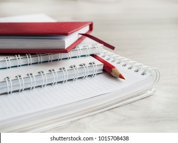 Office accessories: a red notepad, a white notepad and red pencil on a wooden gray desk. Back to school. Close-up. Top view. Copy space