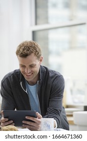 An Office Or Apartment Interior In New York City. A Man In A Sweatshirt Top Using A Digital Pad. Leaning On A Breakfast Bar.