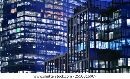 Office building in the evening with lightened workspaces. Modern, glazed skyscraper in financial district. Late hours in the office.