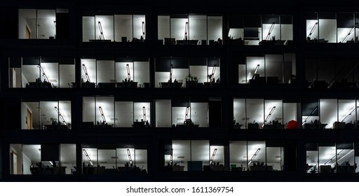 Office Building Exterior At Night With Interior Lights On. Empty Offices With Red Umbrella Behind The Window.