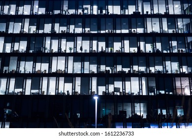 Office Building At Night. Late Night At Work. Glass Curtain Wall Office Building. Office Building Exterior In The Late Evening With Interior Lights On. Evening Facade Of An Office Building.