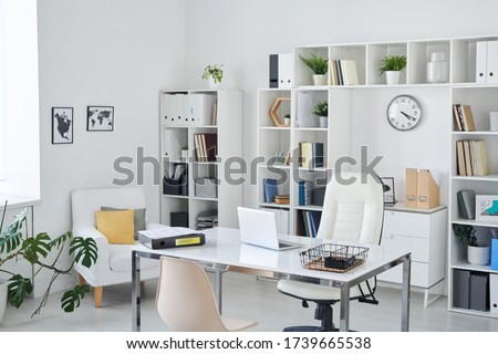 Office of business person with desk, armchair of professional, chair for clients, shelves, clock, green plant and two pictures on wall