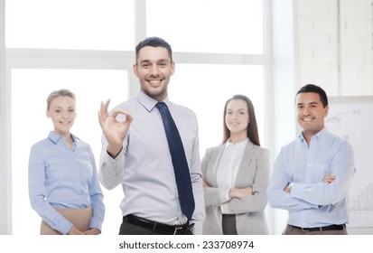 office, business, and teamwork concept - friendly young smiling businessman with team on back showing ok-sign - Powered by Shutterstock