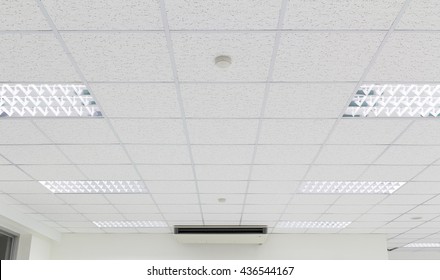 Office Ceiling In Perspective With White Texture Of Acoustic Gypsum Plasterboard, Lighting Fixtures Or Fluorescent Panel Light Suspended On Square Grid Structure. Interior Modern Building Background.