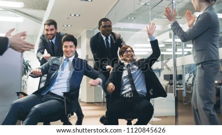 Office Chair Race Four Funny Multi Ethnic Businessmen Ride Chairs in the Corporate Building Hallway. Colleagues Cheer and Applaud. Celebrate Closing of the Deal.