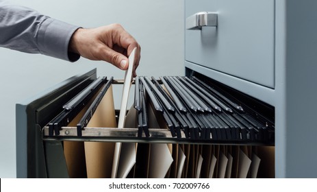 Office clerk searching for files into a filing cabinet drawer close up, business administration and data storage concept - Shutterstock ID 702009766