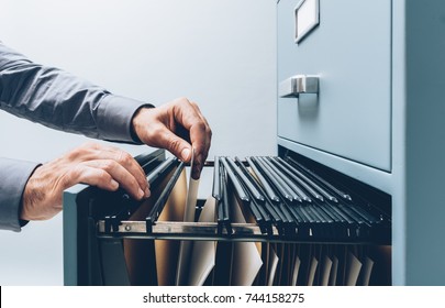 Office clerk searching for files into a filing cabinet drawer close up, business administration and data storage concept - Shutterstock ID 744158275
