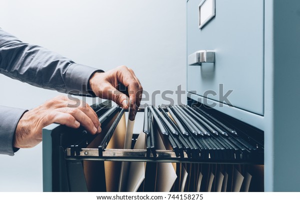 Office\
clerk searching for files into a filing cabinet drawer close up,\
business administration and data storage\
concept