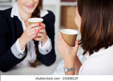 Office coffee break with two female colleagues sitting chatting over cups of coffee