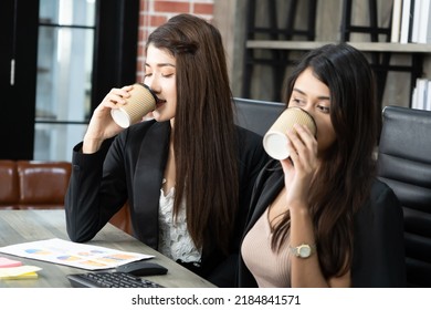 Office Coffee Break With Two Female Colleagues Sitting Chatting Over Cups Of Coffee. Asian Business Woman Holding Coffee Cup In Office.