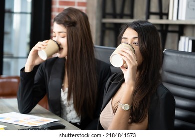 Office Coffee Break With Two Female Colleagues Sitting Chatting Over Cups Of Coffee. Asian Business Woman Holding Coffee Cup In Office.