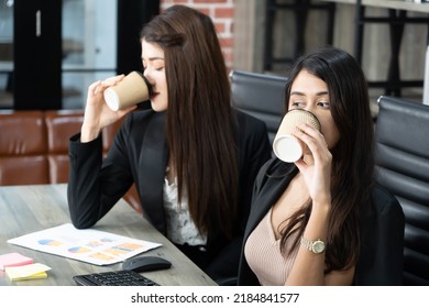 Office Coffee Break With Two Female Colleagues Sitting Chatting Over Cups Of Coffee. Asian Business Woman Holding Coffee Cup In Office.