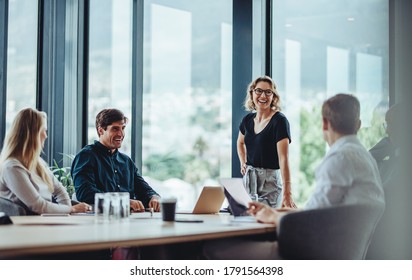 Office colleagues having casual discussion during meeting in conference room. Group of men and women sitting in conference room and smiling.