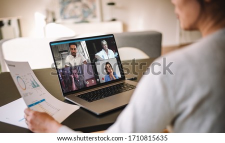 Office colleagues having a video call to discuss few financial reports. Business people working from home having a video conference. Over the shoulder view.