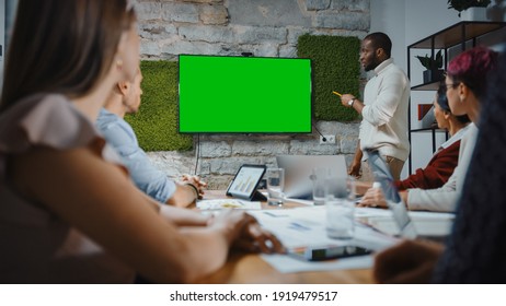 Office Conference Room Meeting: Black Chief Company Strategist Doing Green Screen TV Presentation To A Diverse Team Of Multi-Ethnic Businesspeople. Using Chroma Key Wall TV Monitor