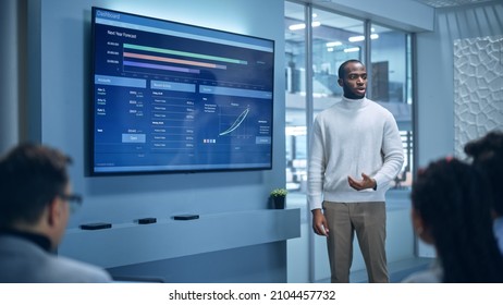 Office Conference Room Meeting Presentation: Black Businessman Talks, Uses Wall TV to Show Company Growth with Big Data Analysis, Graphs, Charts, Infographics. Multi-Ethnic e-Commerce Startup Workers