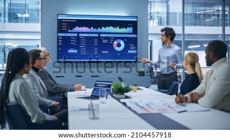 Office Conference Room Meeting Presentation: Latin Businessman Talks, Uses Wall TV to Show Company Growth with Big Data Analysis, Graphs, Charts, Infographics. Multi-Ethnic e-Commerce Startup Workers