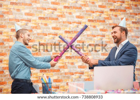 In the office at a corporate party, men are fooled with sticks from under confetti.