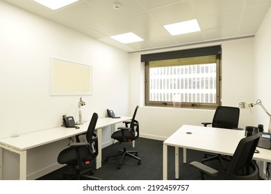 Office Cubicle With A Small White Double Table With Telephones, Black Swivel Chairs, A Window With A View And A Dark Gray Carpet Floor