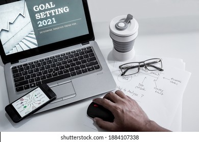 Office desk for Goal Setting 2021 presentation set up with notebook, smartphone, reading glasses, paper note and tumblr