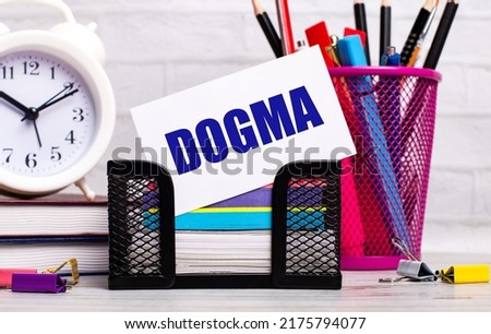 The office desk has diaries, an alarm clock, stationery, and a white card with the text DOGMA. Business concept.