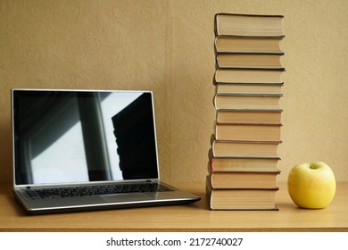 Office Desk With Laptop Blank Screen, Green Apple And Stack Of Books. Student Workspace With Laptop Computer Empty Screen Mockup On Wooden Table
