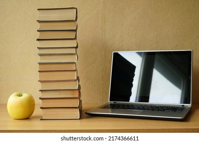 Office Desk With Laptop Blank Screen, Green Apple And Stack Of Books. Student Workspace With Laptop Computer Empty Screen Mockup On Wooden Table
