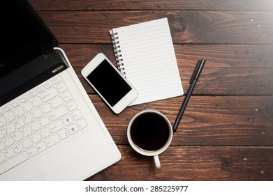 Office desk with laptop computer, notebook, mobile smartphone and coffee cup on wood,morning light