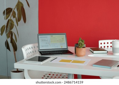 Office desk with laptop, stationery, digital tablet, coffee cup and plant in modern workspace with red wall - Powered by Shutterstock