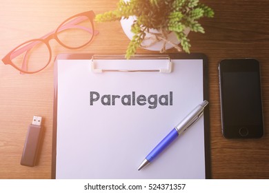 Office Desk With A Paper Written Paralegal With Pen, Glass, Smartphone And A Thumb Drive