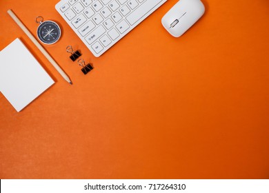 Office desk table of Business workplace and business objects of keyboard,mouse,white paper,notebook,pencil,compass on orange background