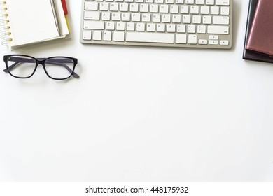 Office desk table with computer keyboard, office supplies on white background Top view / Image of White Office Desk with Computer Keyboard Pen and Notepad from above sepia toned.