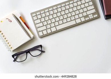 Office desk table with computer keyboard, office supplies on white background Top view / Image of White Office Desk with Computer Keyboard Pen and Notepad from above sepia toned.