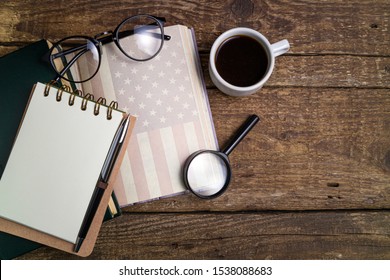 Office Desk Table With Old Book, Cup Of Coffee, American Flag On Book, Pen, Notebook And Magnifier. Goal, Plan, Strategy, Politics, International Relations, Economics, American History, Education
