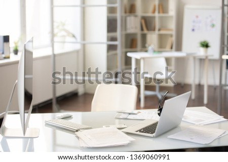 Office desk with two computers on table with report papers, hands-free device on laptop