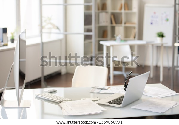 Office desk with two computers on table\
with report papers, hands-free device on\
laptop