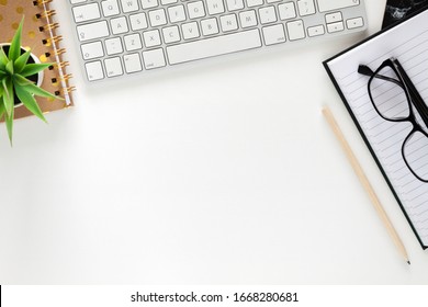 Office desk with white empty space for text. Copy space. Imac keyboard, open notebook, glasses and plant. Office accessories.
