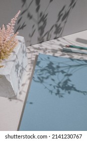 Office Desk Workspace With Blank Blue Note Pad. Leaves Shadows Reflected On Surface.