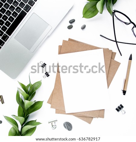 Office desk workspace with paper blank, green leaves and office supplies. Laptop, glasses on white background. Flat composition for magazines, websites, social media.  Flat lay, top view.