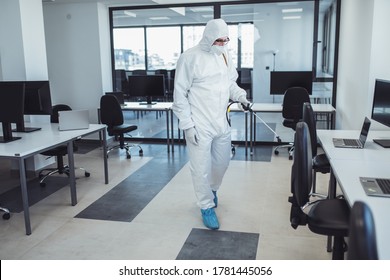 Office Disinfection During COVID-19 Pandemic. Man In Protective Suit And Face Mask Spraying For Disinfection In The Office