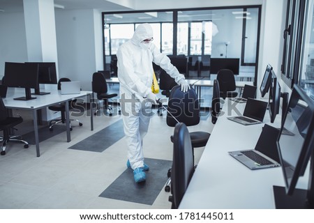 Office disinfection during COVID-19 pandemic. Man in protective suit and face mask spraying for disinfection in the office