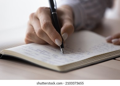 Office employee planning workday, writing list of tasks in notebook, workbook, agenda. Writer, student making notes for remembering, preparing article, essay. Female hand with pen close up