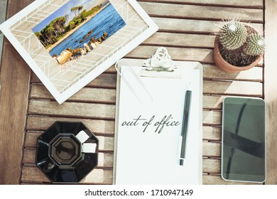 Office Flat Lay With A Holiday Photo Coffee A Smartphone And A Cactus Words Out Of Office Written In English On A Notepad With Her Wooden Desk Pen